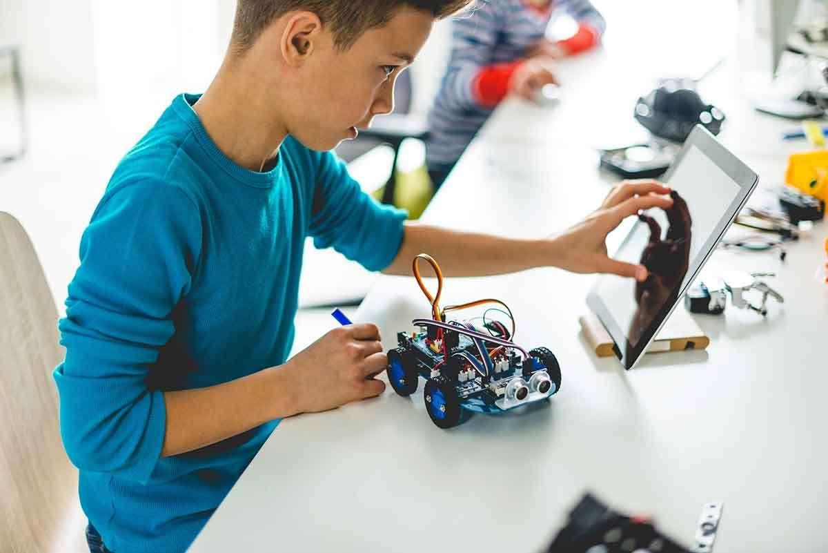 A boy constructs a car in class using an electronic gadget


