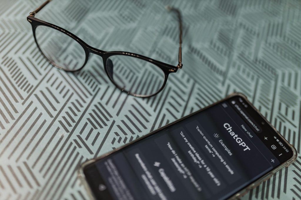 Glasses lay next to a phone where ChatGPT homepage is open