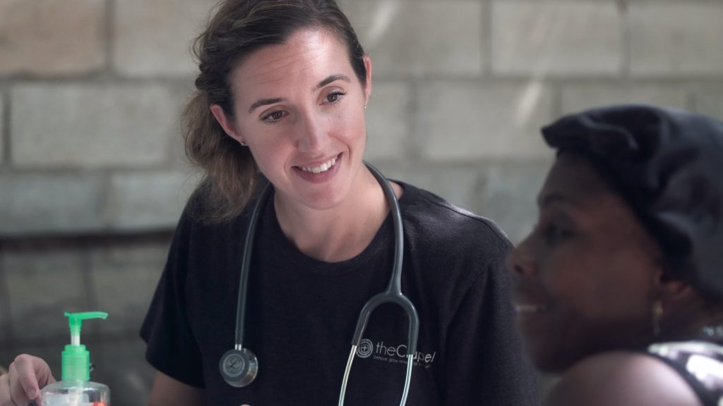 A female doctor talks to a person outside and smiles