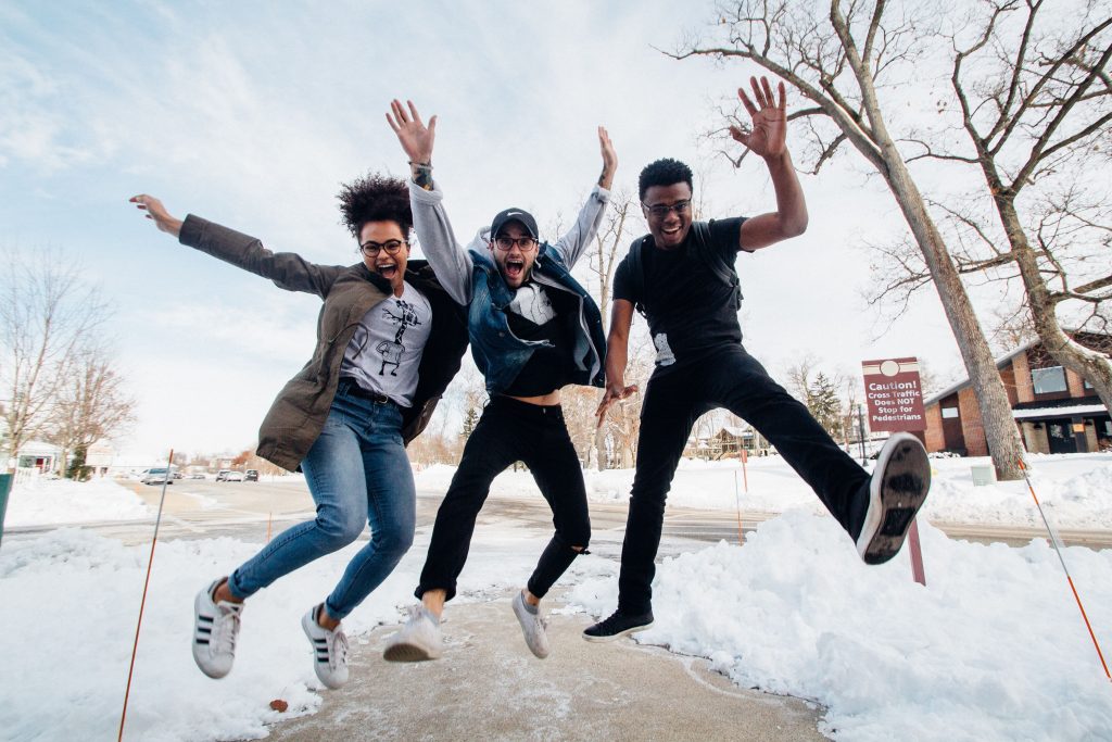 A small group of young people jump up outside during winter